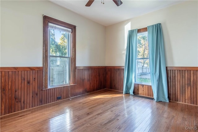 unfurnished room featuring ceiling fan, light hardwood / wood-style floors, and wooden walls