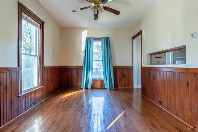 empty room featuring hardwood / wood-style flooring, ceiling fan, and wood walls