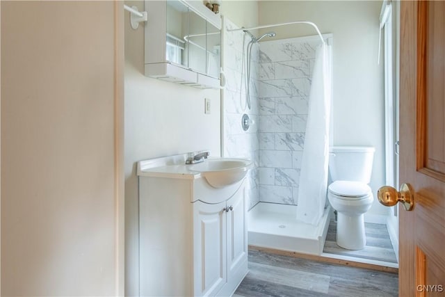 bathroom with tiled shower, wood-type flooring, vanity, and toilet