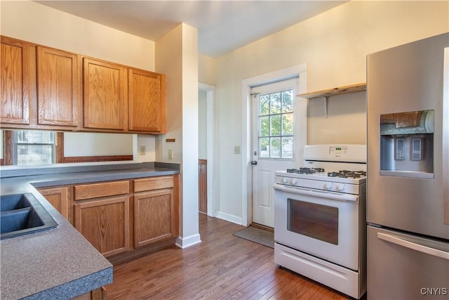 kitchen with stainless steel fridge with ice dispenser, dark hardwood / wood-style floors, white gas stove, and sink