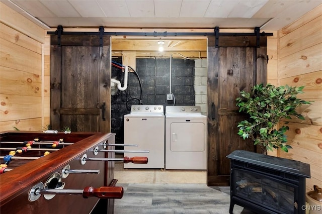 laundry room featuring light wood-type flooring, a barn door, wooden walls, and washing machine and clothes dryer