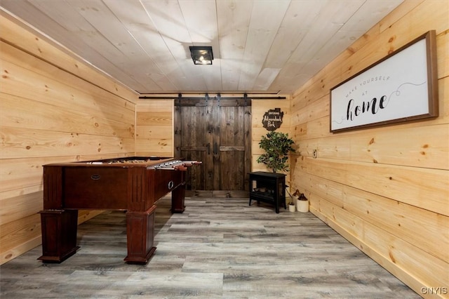 game room with hardwood / wood-style flooring, wood walls, and a barn door