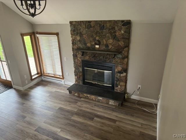 living room with a chandelier, a stone fireplace, wood-type flooring, and vaulted ceiling