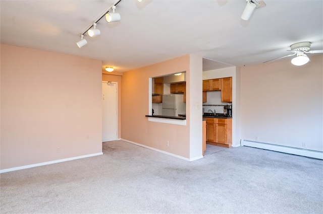 unfurnished living room featuring a baseboard heating unit, light colored carpet, rail lighting, and ceiling fan