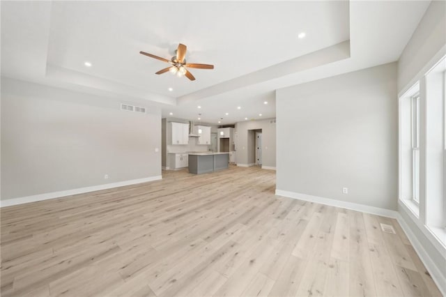 unfurnished living room featuring light hardwood / wood-style floors, a tray ceiling, and ceiling fan