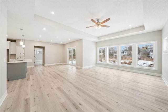 unfurnished living room featuring light wood-type flooring, ceiling fan, a tray ceiling, and sink