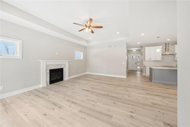 unfurnished living room featuring ceiling fan, a fireplace, a tray ceiling, and light hardwood / wood-style floors