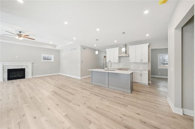 kitchen with ceiling fan, a kitchen island with sink, hanging light fixtures, white cabinets, and sink