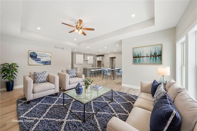 living room with ceiling fan, light hardwood / wood-style flooring, and a raised ceiling