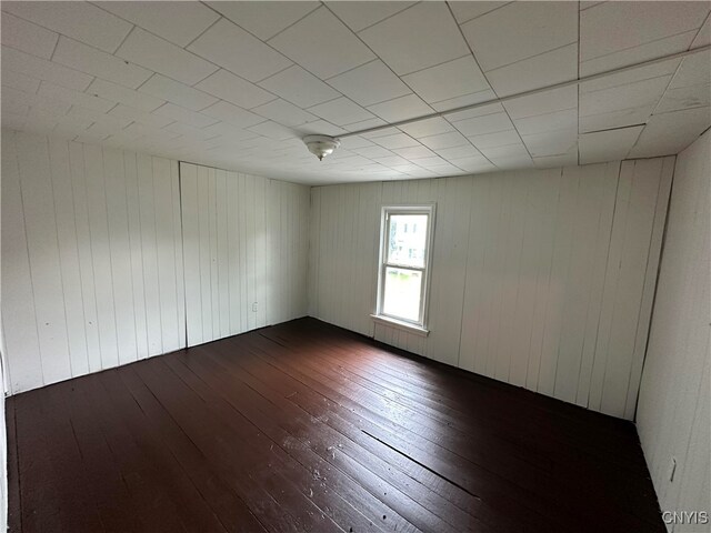 unfurnished room with wooden walls and dark hardwood / wood-style flooring