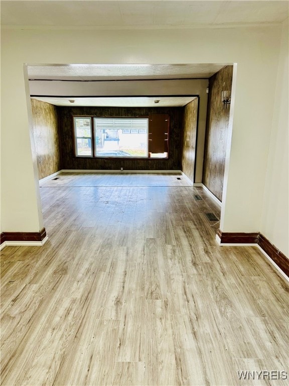 empty room with light wood-type flooring and wooden walls