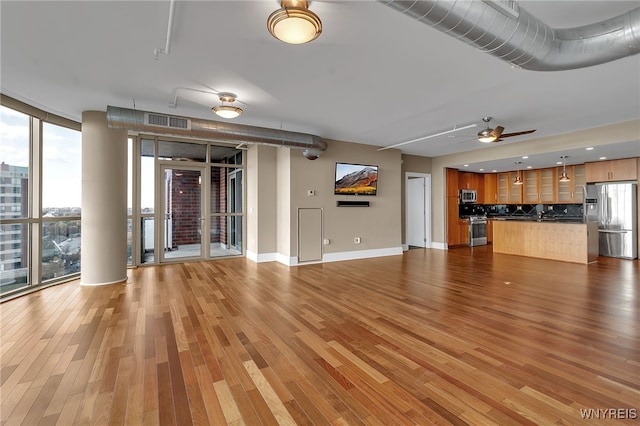 unfurnished living room featuring ceiling fan, a wall of windows, and wood-type flooring