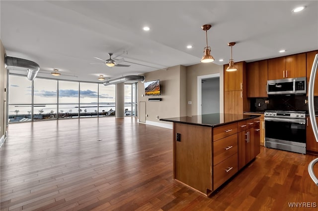 kitchen with decorative light fixtures, a center island, dark hardwood / wood-style floors, a wall of windows, and stainless steel appliances