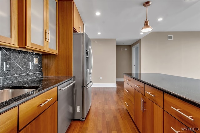 kitchen featuring dark stone countertops, hanging light fixtures, stainless steel appliances, decorative backsplash, and light wood-type flooring