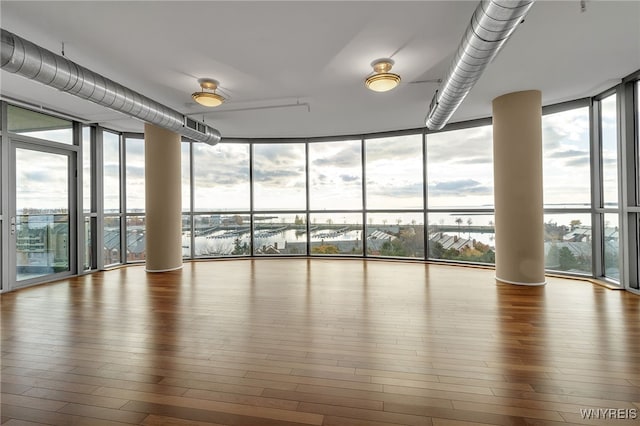 interior space with expansive windows, a water view, plenty of natural light, and hardwood / wood-style floors