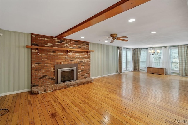 unfurnished living room featuring a fireplace, ceiling fan with notable chandelier, wooden walls, beamed ceiling, and light hardwood / wood-style floors