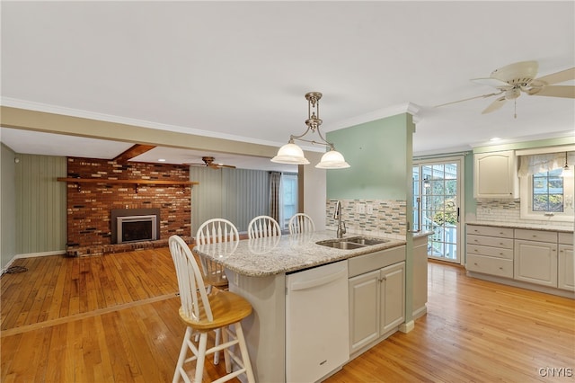 kitchen with backsplash, a brick fireplace, white dishwasher, sink, and decorative light fixtures