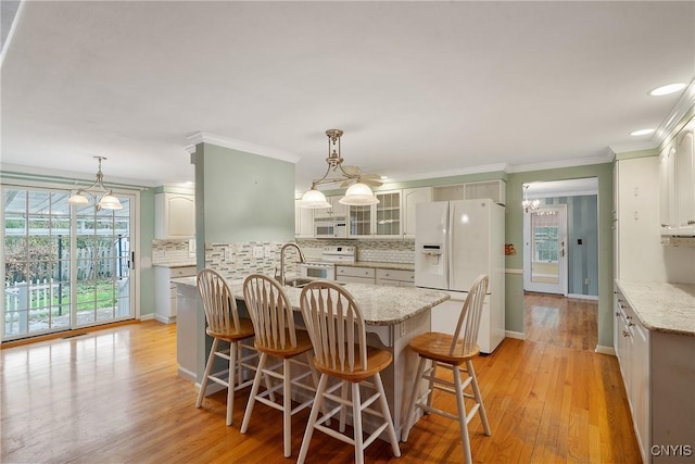 kitchen with light wood-type flooring, white appliances, decorative light fixtures, and backsplash