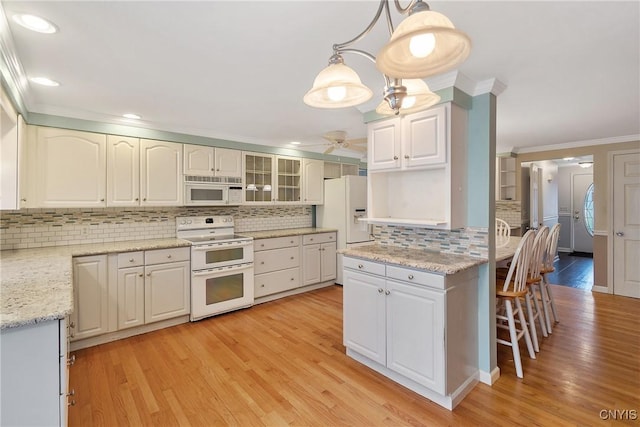 kitchen with white cabinets, pendant lighting, white appliances, and light hardwood / wood-style floors