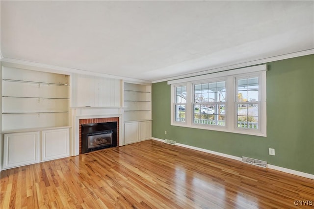 unfurnished living room featuring built in features, light hardwood / wood-style floors, a brick fireplace, and crown molding