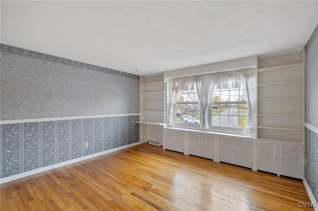 unfurnished room featuring hardwood / wood-style floors and built in shelves