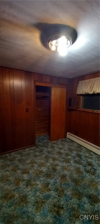 empty room featuring wood walls, baseboard heating, and dark carpet