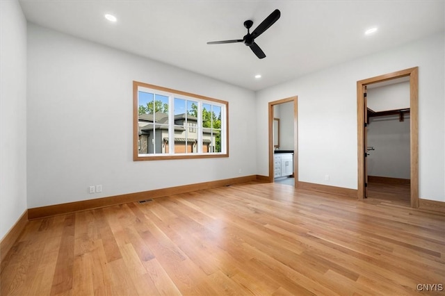 unfurnished bedroom with a walk in closet, a closet, ceiling fan, and light hardwood / wood-style floors