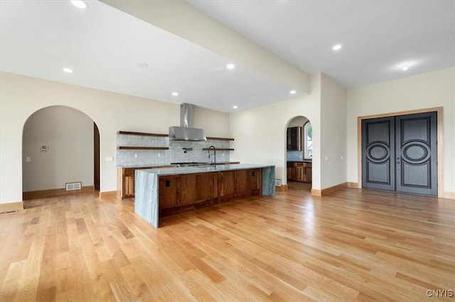 kitchen featuring light hardwood / wood-style floors, a large island with sink, decorative backsplash, and wall chimney exhaust hood