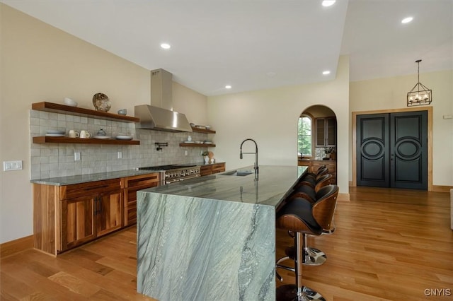 interior space with wall chimney exhaust hood, decorative light fixtures, light wood-type flooring, backsplash, and sink