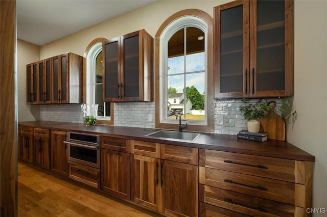 kitchen featuring sink, oven, light wood-type flooring, and tasteful backsplash