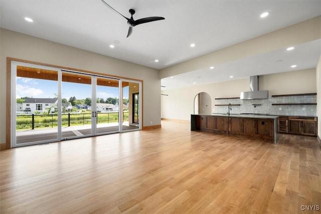 kitchen featuring light wood-type flooring, a center island, ceiling fan, wall chimney range hood, and backsplash