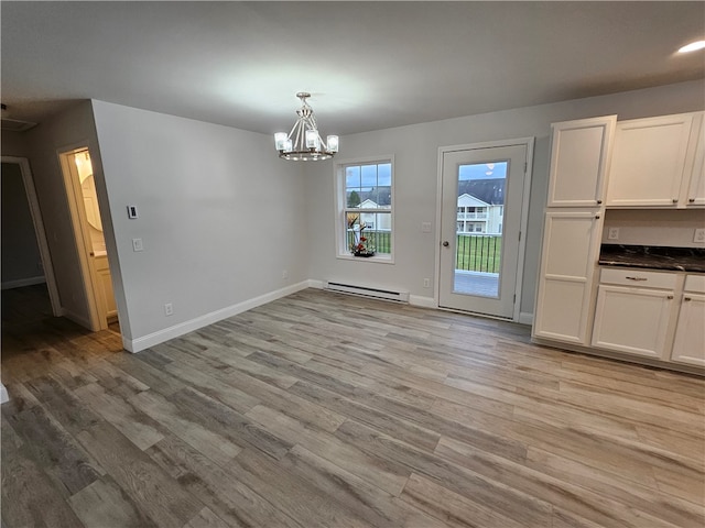 unfurnished dining area with an inviting chandelier, light hardwood / wood-style flooring, and a baseboard heating unit