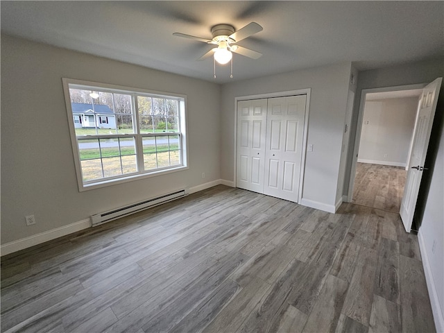 unfurnished bedroom featuring light hardwood / wood-style flooring, a closet, ceiling fan, and a baseboard heating unit