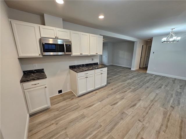 kitchen with dark stone counters, white cabinetry, a chandelier, and light wood-type flooring