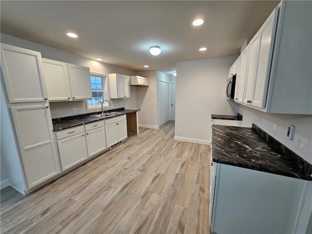 kitchen with dark stone counters, sink, light hardwood / wood-style floors, and white cabinets