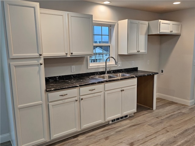 kitchen with dark stone counters, light hardwood / wood-style floors, white cabinetry, and sink