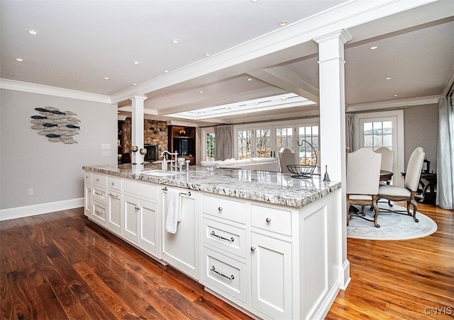 kitchen featuring dark wood-type flooring, light stone counters, sink, decorative columns, and white cabinetry