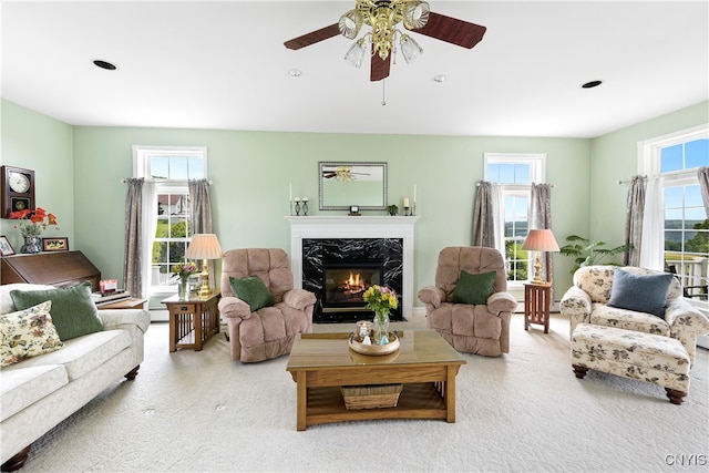 carpeted living room with a high end fireplace and ceiling fan