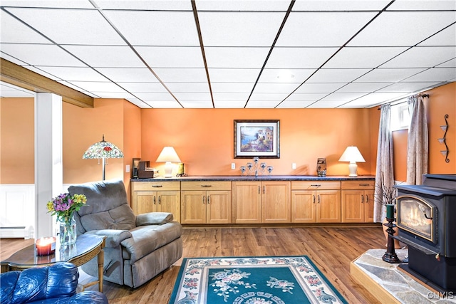 interior space with a wood stove, hardwood / wood-style floors, a baseboard radiator, and a paneled ceiling