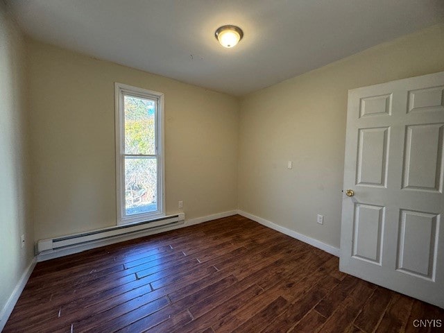 spare room featuring baseboard heating and dark hardwood / wood-style flooring