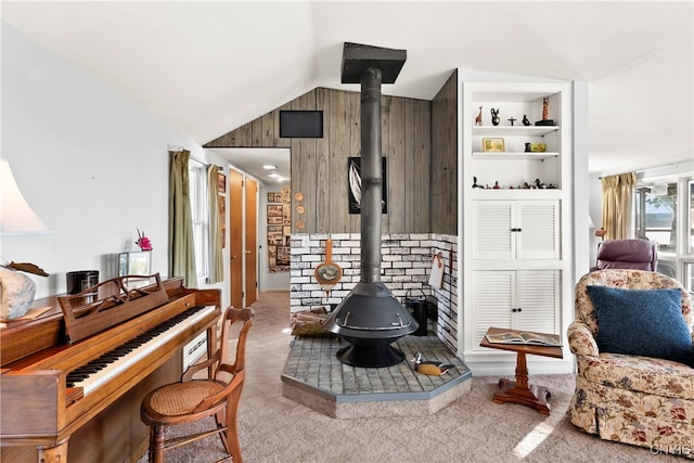 interior space with built in shelves, a wood stove, wooden walls, lofted ceiling, and light colored carpet