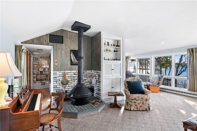 carpeted living room with wood walls, a baseboard radiator, a wood stove, and vaulted ceiling