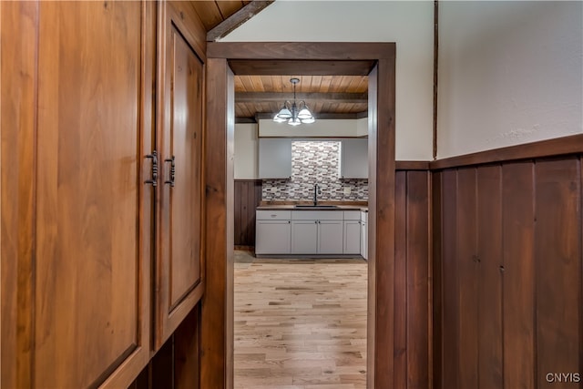 corridor featuring light wood-type flooring, beamed ceiling, sink, and wooden ceiling