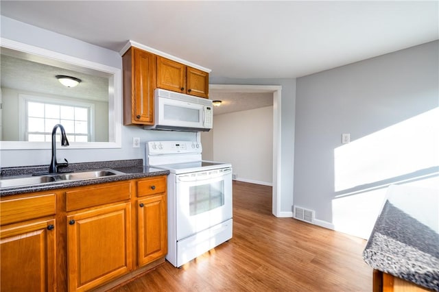 kitchen with brown cabinets, visible vents, a sink, white appliances, and light wood-style flooring