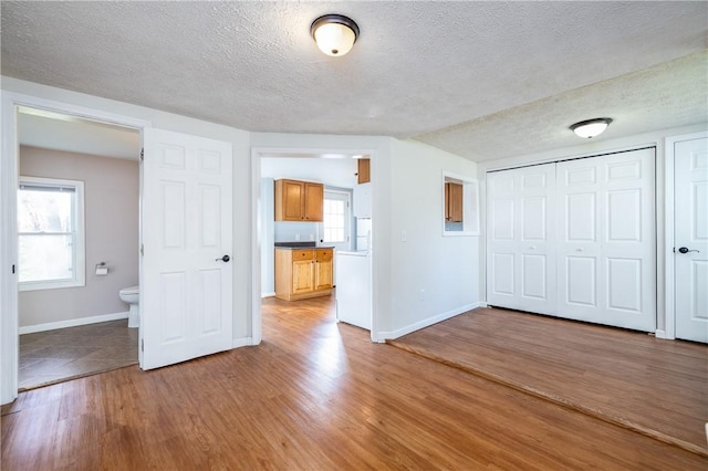 unfurnished bedroom featuring a textured ceiling, a closet, multiple windows, light wood finished floors, and baseboards