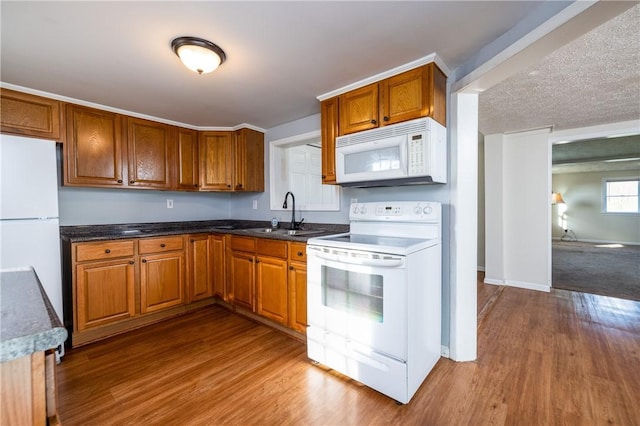 kitchen featuring brown cabinets, wood finished floors, a sink, and white appliances