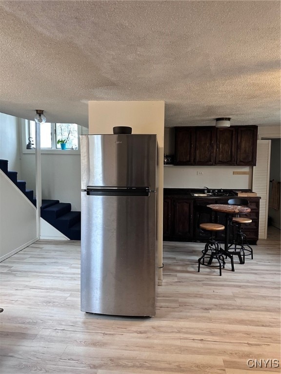 kitchen with light hardwood / wood-style floors, stainless steel refrigerator, a textured ceiling, and dark brown cabinets