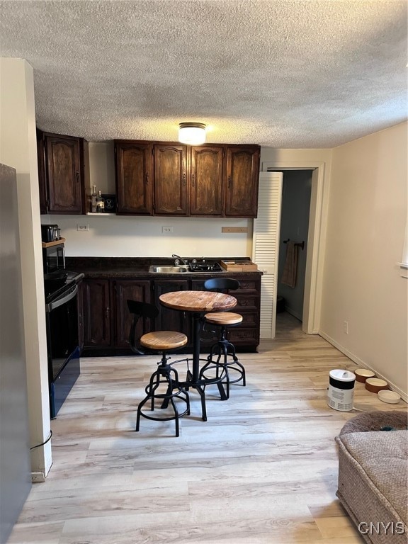 kitchen featuring black appliances, light wood-type flooring, sink, and dark brown cabinets