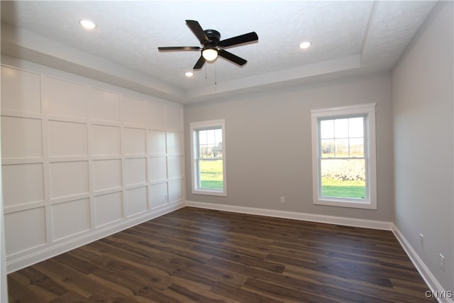 empty room featuring dark hardwood / wood-style flooring, a textured ceiling, a tray ceiling, and plenty of natural light