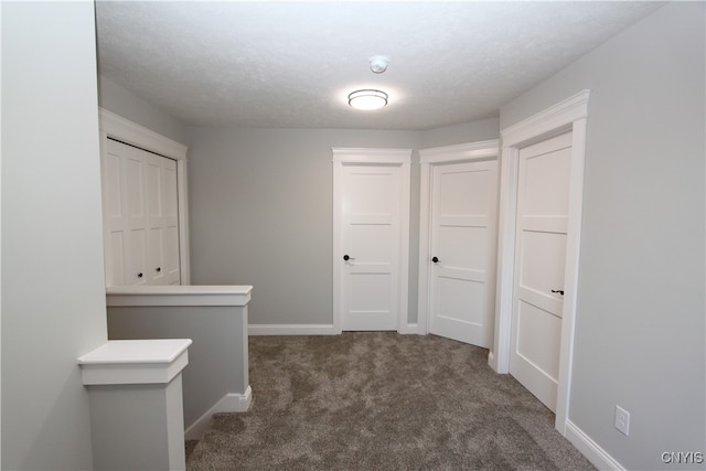 corridor featuring a textured ceiling and dark carpet